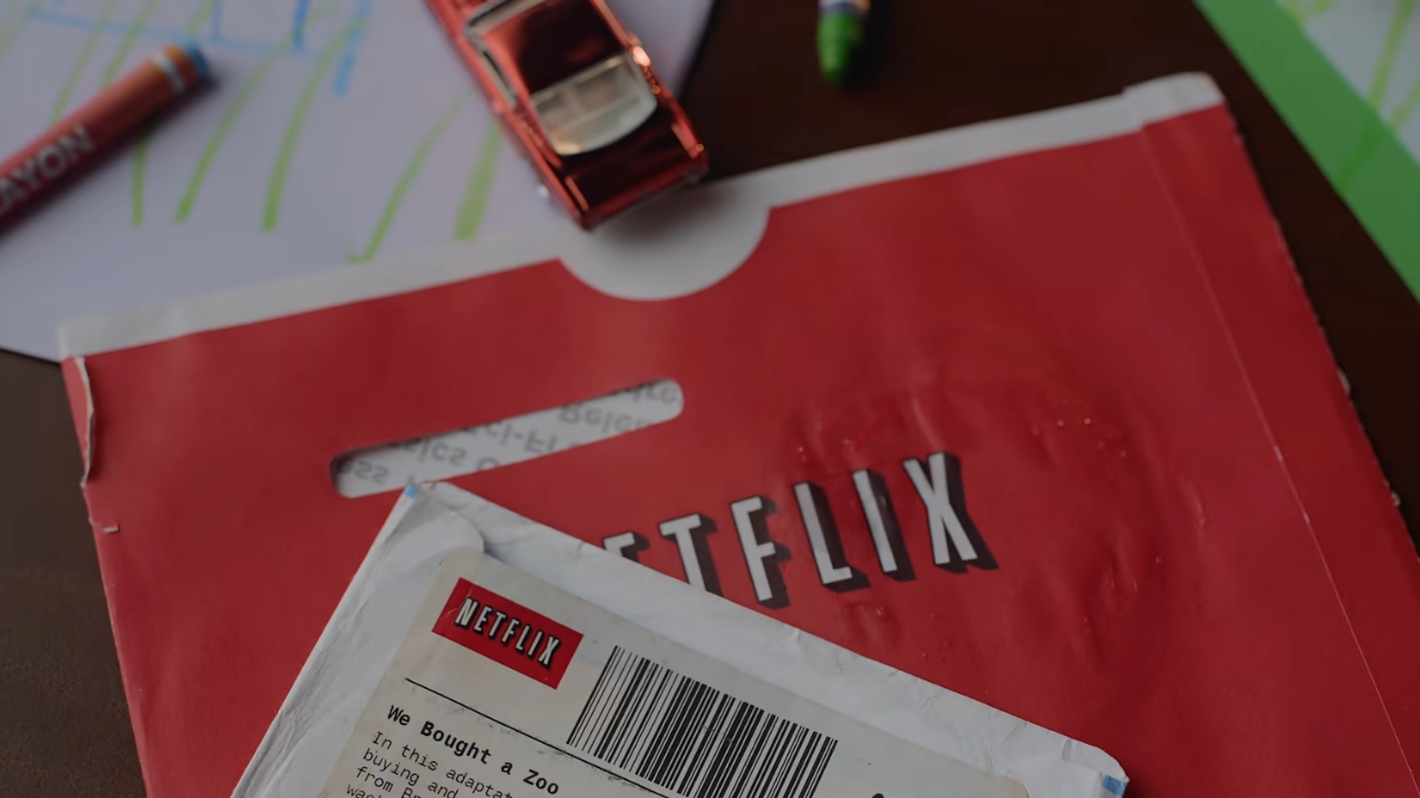 A red Netflix DVD envelope sits beneath a white mailer on a desk.