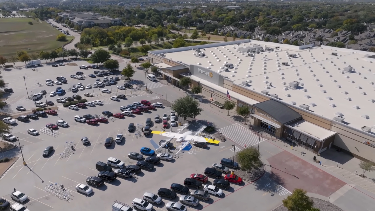 A delivery drone flies above a Walmart parking lot filled with cars.