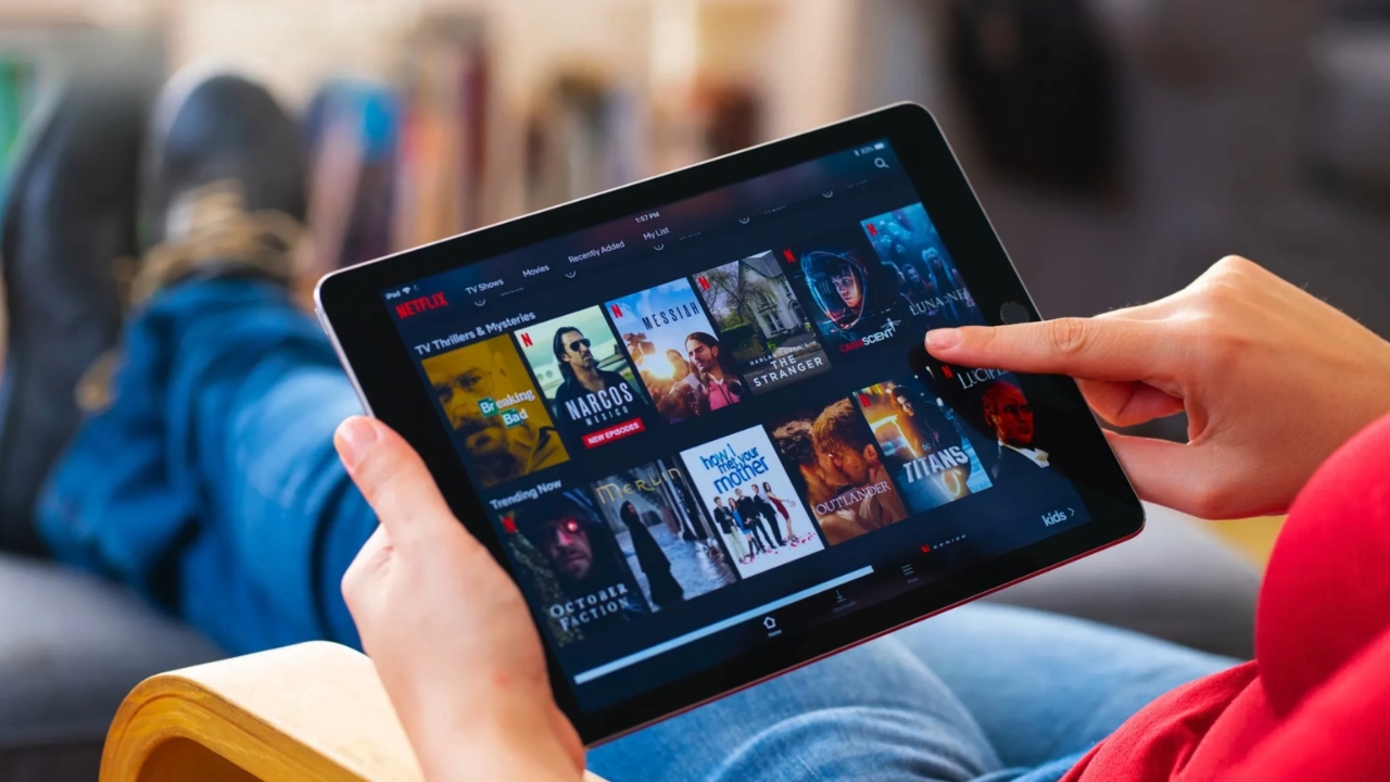 A person uses a tablet to browse Netflix shows and movies while seated on a couch.